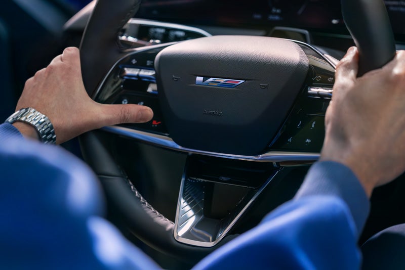 Close-up of a Man About to Press the V-Button on the 2026 OPTIQ-V Steering Wheel | Denny Menholt Cadillac in Rapid City SD